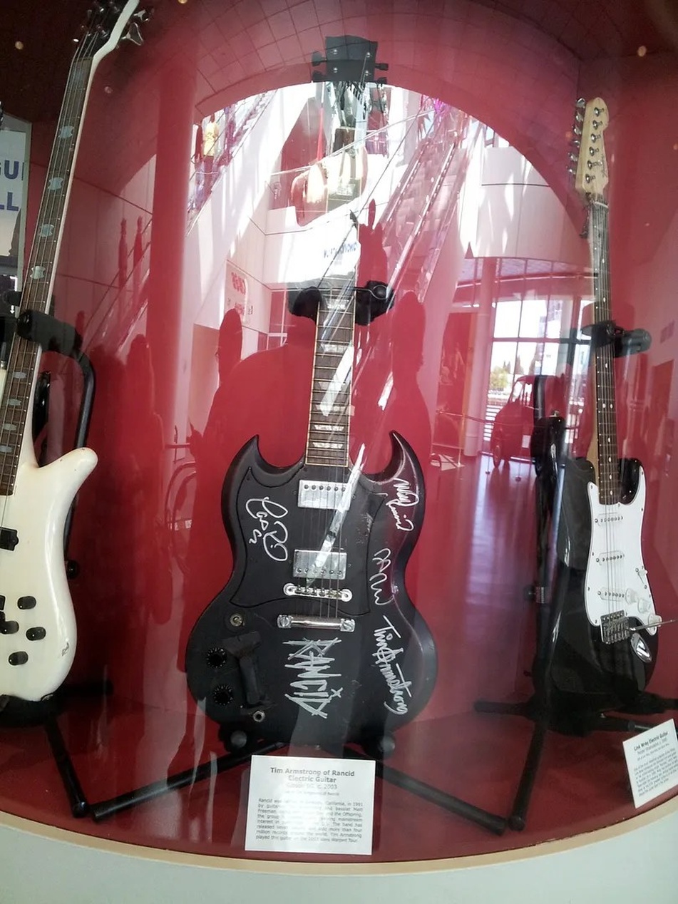 Une vitrine contenant plusieurs guitares électriques, dont une guitare noire signée, illustrant le matériel précieux transporté en tournée.